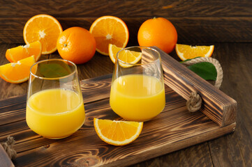 Fresh orange juice in glasses with cut oranges on wooden tray. Rustic still life with citrus fruits