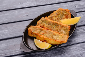 Fried fish with a piece of lemon over rustic wooden table. Delicious idea for dinner.