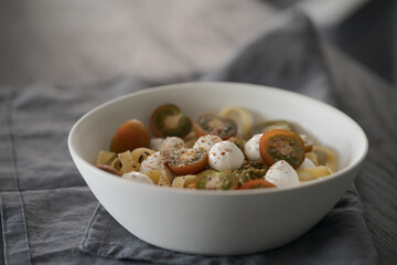 Fettuccine with mozzarella, tomatoes and pesto in white bowl on black table