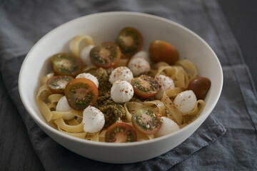 Fettuccine with mozzarella, tomatoes and pesto in white bowl on black table