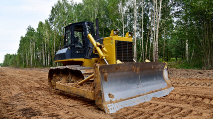 Dozer during clearing forest for construction new road . Yellow Bulldozer at forestry work Earth-moving equipment at road work, land clearing, grading, pool excavation, utility trenching © MaxSafaniuk