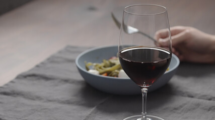 man eatings fettuccine with pesto, tomatoes and mozzarella with glass of red wine