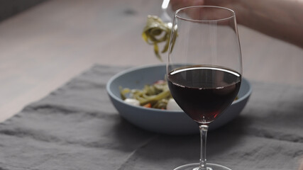 man eatings fettuccine with pesto, tomatoes and mozzarella with glass of red wine