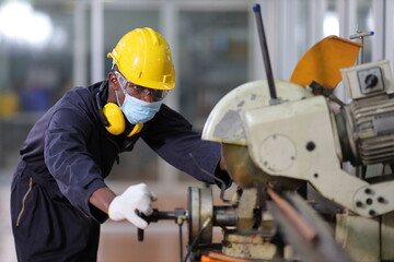 African American mechanic engineer worker wearing facial mask is choosing copper tube for sawing while working in coolant factory under new normal policy during covid-19 pandemic with copy space