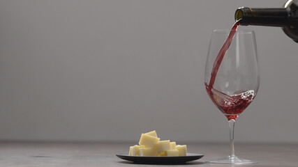 pour red wine into wineglass with hard cheese on background on wood table