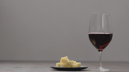 red wine into wineglass with hard cheese on background on wood table