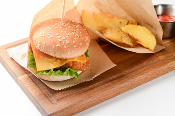 Hamburger with fries and sauce. Juicy burger on a wooden board over white background. Fast food, junk food concept.