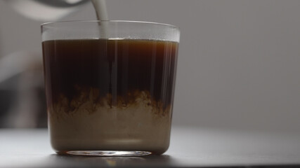 pour cream in coffee in tumbler glass on concrete countertop with copy space