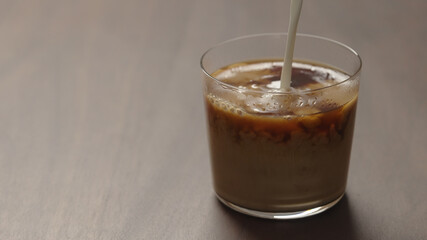 pour cream in coffee in tumbler glass on walnut wood table with copy space