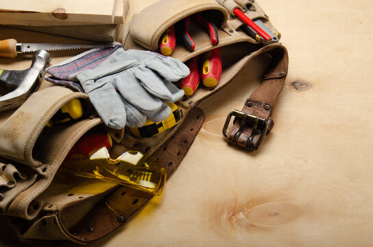 Tool belt with carpenter tools and protective wear on plywood sheet