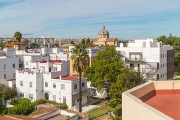 Fototapeta na wymiar View of the rooftops of Seville on a beautiful sunny morning (Andalusia, Spain). White buildings with red-painted roofs on the horizon. Cityscape overlooking a large church.