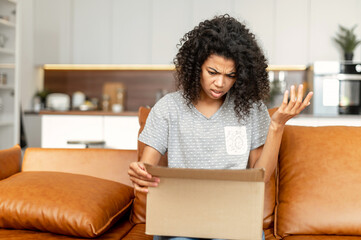 Disappointed African-American woman looking Inside cardboard box, got a wrong online order. Sad...