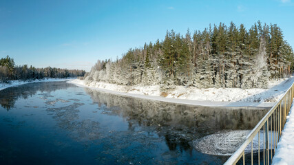 Panoramic winter landscape from the bridge, beautiful frosty trees by the river, slow river flow,...