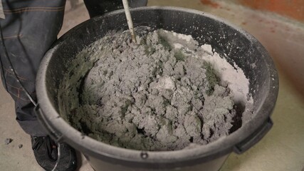 Construction worker mixes leveling compound, putties the floor and prepares the floor for parquet laying. The worker mixes the filling floor in the bucket.