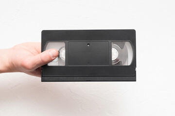 Old black vhs video tape in the male hands on the white background.