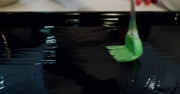 the hands of a young woman anointing the baking tray with sunflower oil.