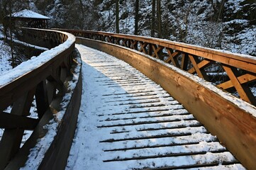 Obraz premium Beautiful snowy wooden bridge with a path for hiking. Winter season with snow and sun.