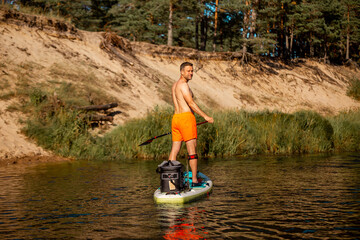 Fototapeta na wymiar A young athletic man rowing with a SUP stand up paddle board in the river. Back view