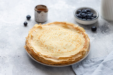 stack of freshly baked thin pancakes, crepes and honey, blueberries in the background. Shrovetide, Maslenitsa holiday concept. Gray background