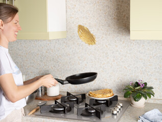 smiling woman flipping hot pancake. The process of making thin pancakes, crepes at home. Shrovetide, Maslenitsa holiday concept. soft focus