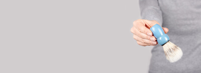 Hand with shaving brush on grey background.