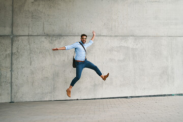 Fototapeta na wymiar Young businessman jumping in joy and looking at camera outdoors in the city