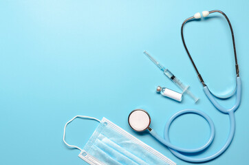 Ampoule with vaccine of COVID-19, syringe and stethoscope on blue background. Flat lay with