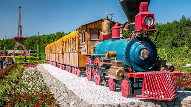 Train at Dubai miracle garden timelapse with over 45 million flowers in a sunny day, United Arab Emirates. Eifel tower model in the backgroung