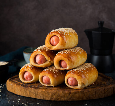 Homemade sausages in dough (pigs in blanket) on a wooden board, dark background