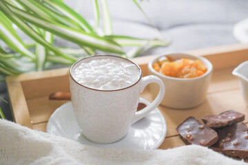 coffee cup and chocolate and orange jam on wooden rack. cozy home. weekend breakfast concept. cosy morning. green plants in the kitchen.