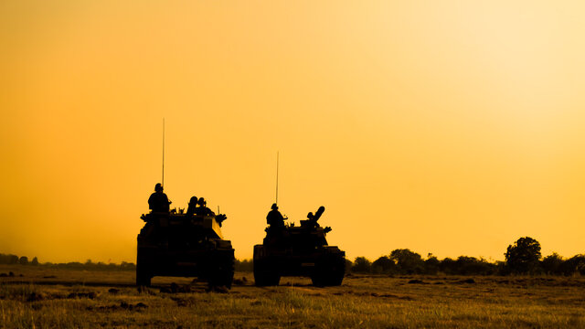 Silhouettes of army soldiers in the fog against a sunset, marines team in action, surrounded fire and smoke, shooting with assault rifle and machine gun, attacking enemy 