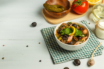 Solyanka, a thick soup made from different types of meat products, is a national Russian dish. In a white bowl, on a light wooden table, with space