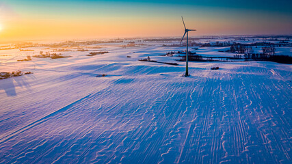 Amazing snowy field and wind turbine at sunrise in winter