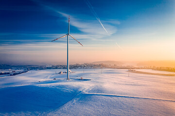 Stunning snowy field and wind turbine at sunrise in winter