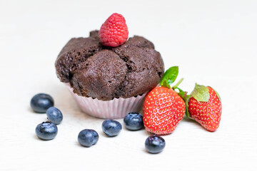 Baked chocolate muffin with juicy berries, strawberries, blueberries, raspberries.
