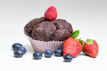 Baked chocolate muffin with juicy berries, strawberries, blueberries, raspberries.