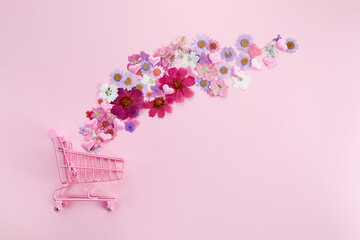 Flowers fly out of the pink shopping cart on a pink background. Season sale, spring shoping...