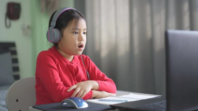 Asian child or kid girl e-learning on computer notebook to wearing headphone and sleepy yawn or bored to video call communication by study online or people learn from home by laptop to back to school