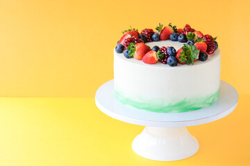 Cake on birthday decorated with strawberry, blueberry, pomegranate, on a yellow background.