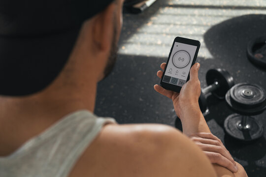 A man with a smart phone in the gym. Looking at the screen of the smart phone. With dumbbells on the floor. health and wellness concept.