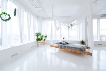 large very bright spacious stylish open plan Bali style apartment with hanging bed and panoramic windows. white floor and walls, simple wooden furniture.