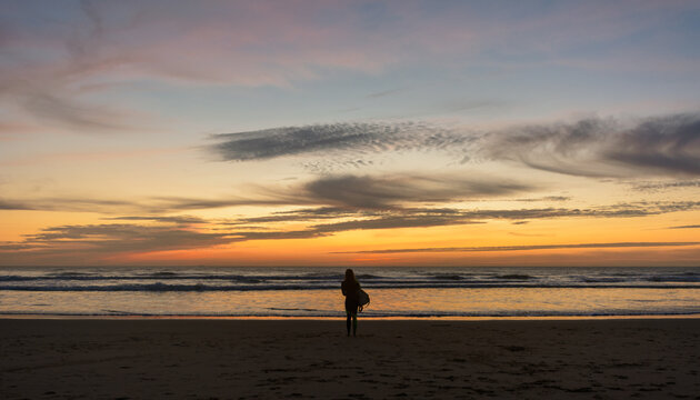 Surfing Sunset. Silhouette of female surfer carrying boards along the sand of a beach