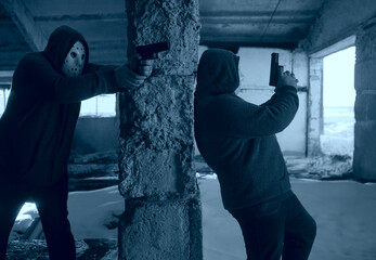 hooded robbers with a gun on old tiled wall background. men wearing white hockey mask and warm...