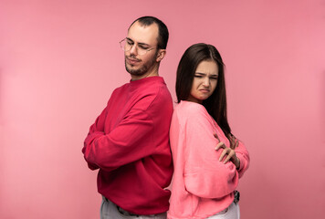Fototapeta premium Photo of attractive couple stands back to back and looks resentful and desperate, isolated over pink background