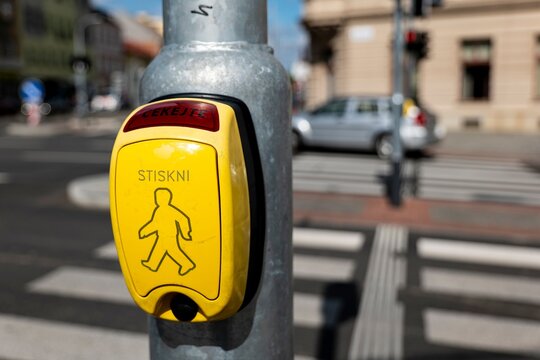 The yellow controller with the text "Press" (Stiskni in Czech language) on pole near the crosswalk with blurred background