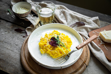 Rustic dinner with risotto all Milanese. Risotto with Saffron and parmesan on white plate on wooden table. 