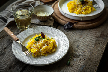 Rustic dinner for two with risotto all Milanese and wine. Risotto with Saffron and parmesan on white plate on wooden table. 