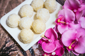 Fototapeta na wymiar coconut candies on a white plate decorated with a pink orchid