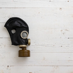 Old vintage gas mask in black on a white wooden background. Side view of a rubber gas mask with a...