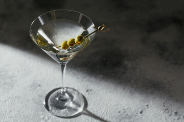 Glass of classic dry martini cocktail with olives on grey stone background.